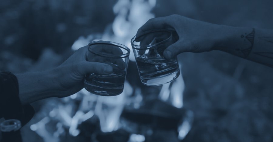 Two glasses of whisky raised by the fire